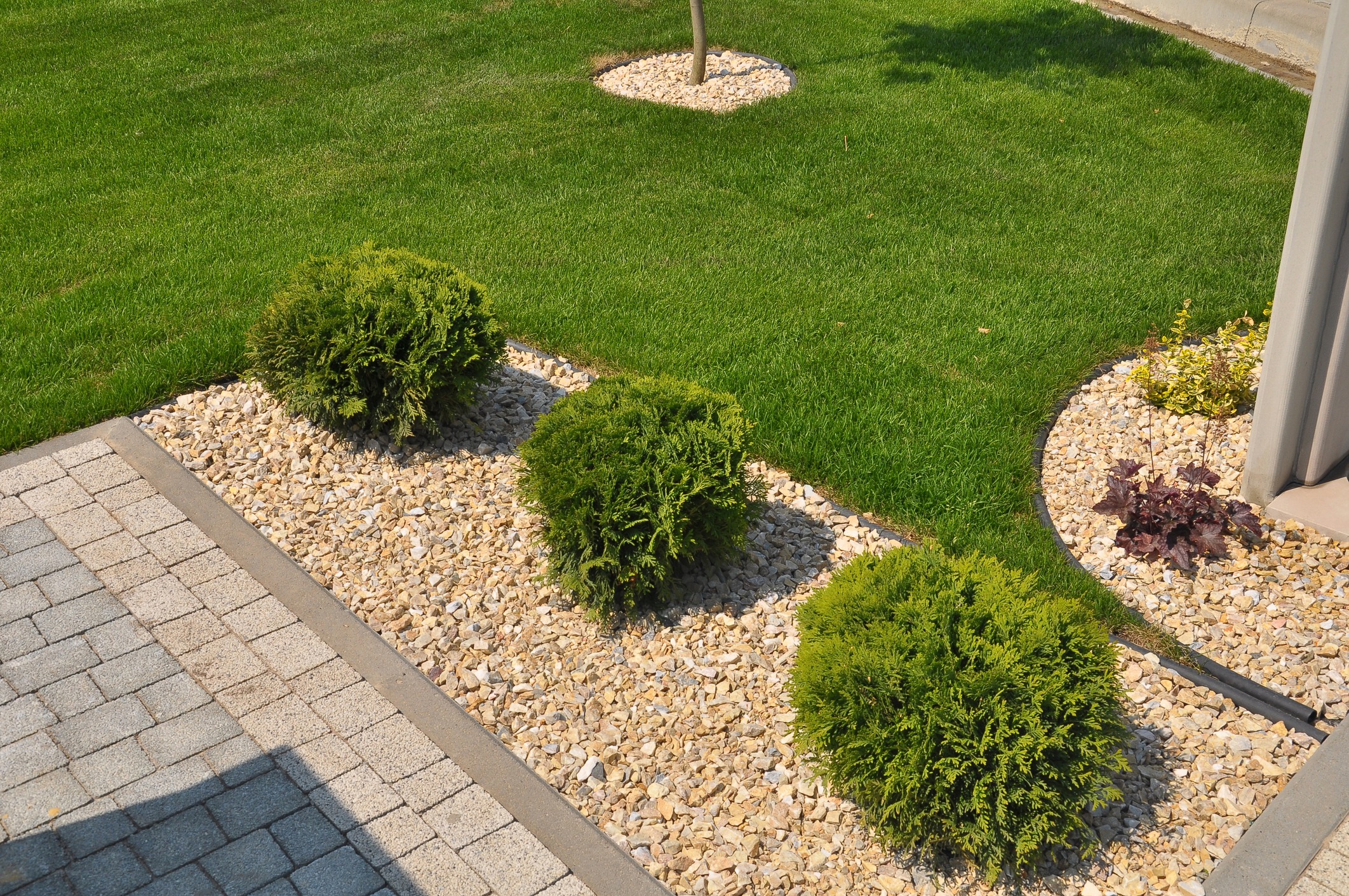 A landscaped garden with green shrubs, grass, and pebble pathways. No visible landmarks or historical buildings are present.