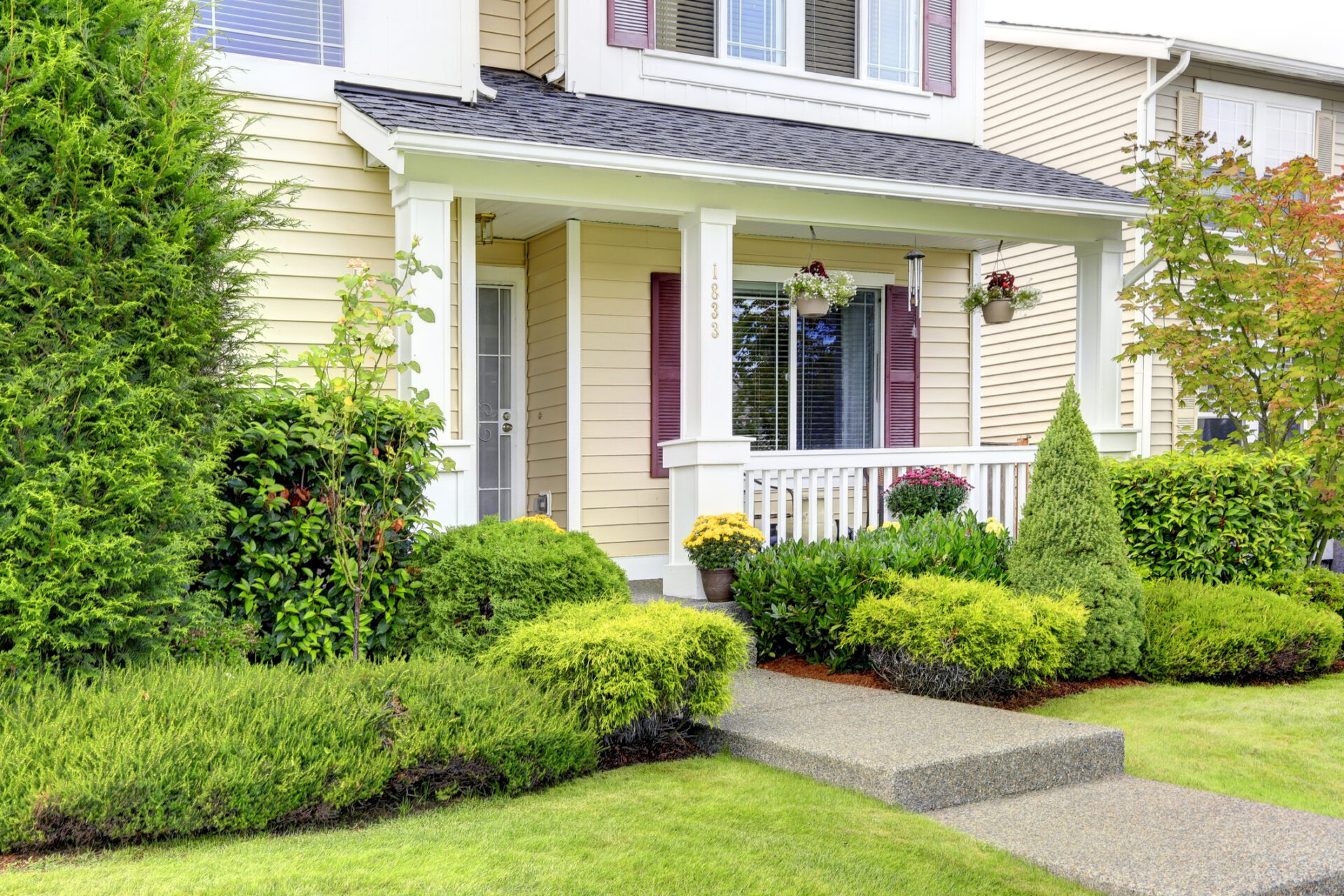 A charming suburban house with a covered porch, vibrant plants, and neatly trimmed hedges adorn the front yard, evoking a sense of tranquility.