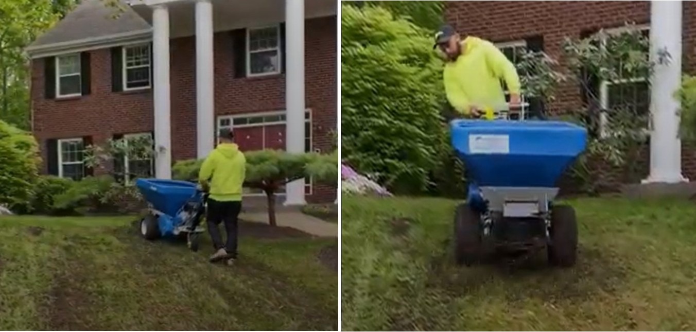 A person in a yellow hoodie operates a blue landscaping machine on a grass lawn in front of a red brick building with columns.